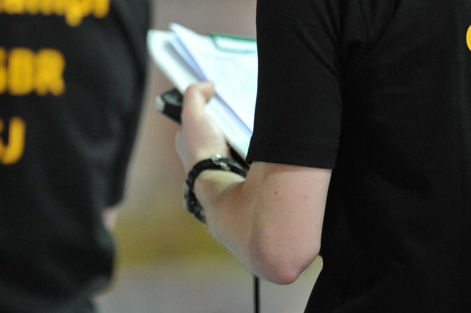 Person in schwarzem T-Shirt hält ein Notizbuch und Stift, im Hintergrund leuchtende Ampeln.